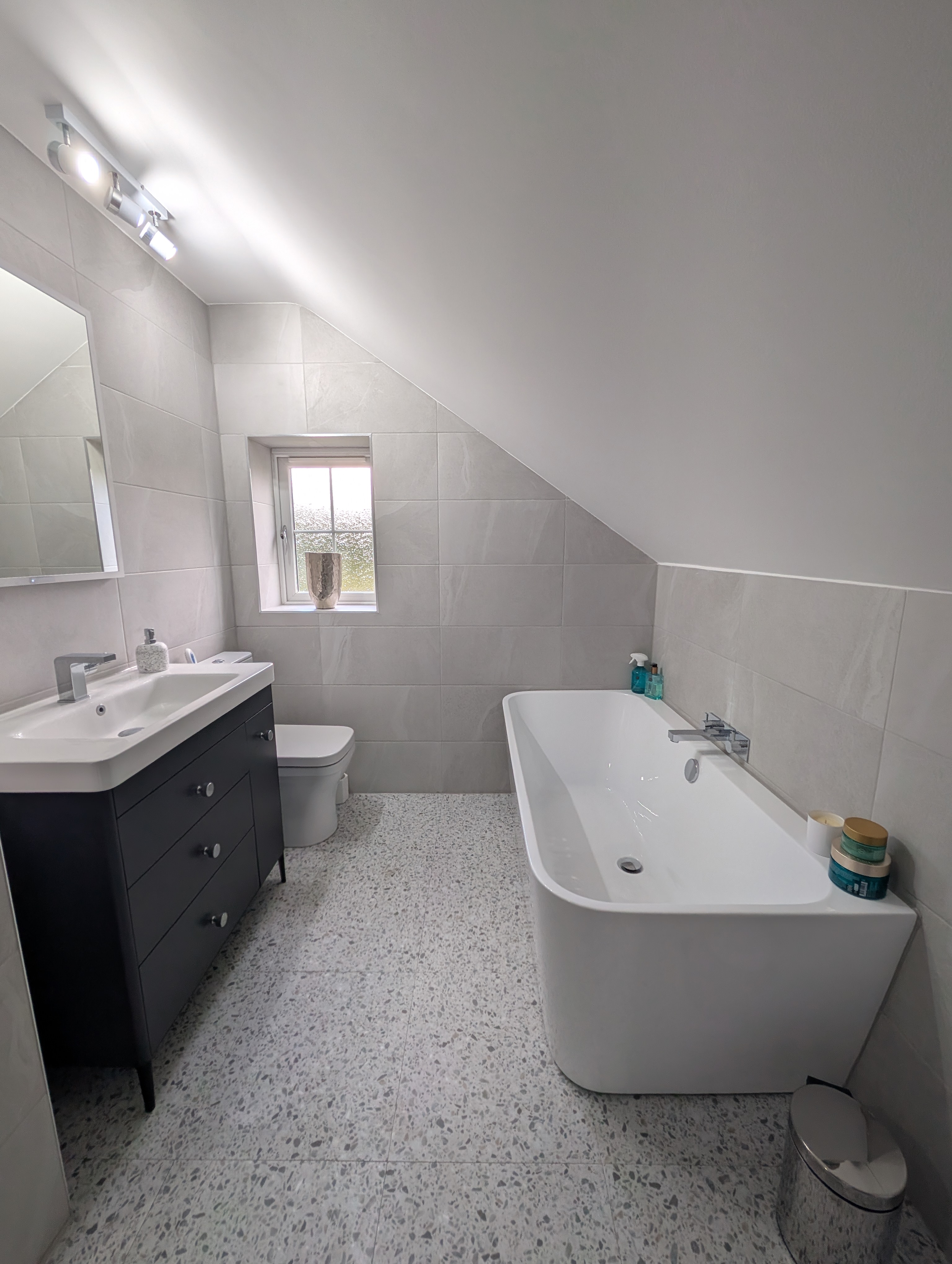 Completed bathroom installation in Stoke-on-Trent with light-grey tiling, freestanding bath and dark vanity